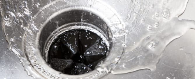 Wide image of a newly installed garbage disposal in a stainless steel sink with water flowing down the drain