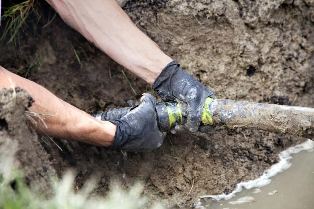 Plumber in black gloves handling sewer line in yard